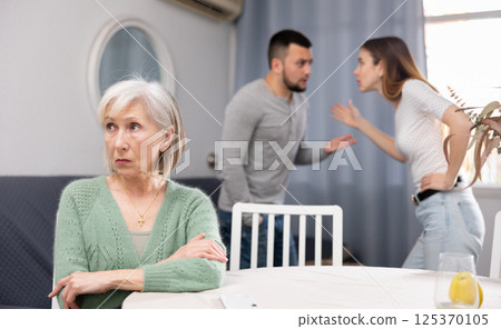 Upset senior woman and quarreling spouses at home Upset senior woman and quarreling spouses at home 125370105