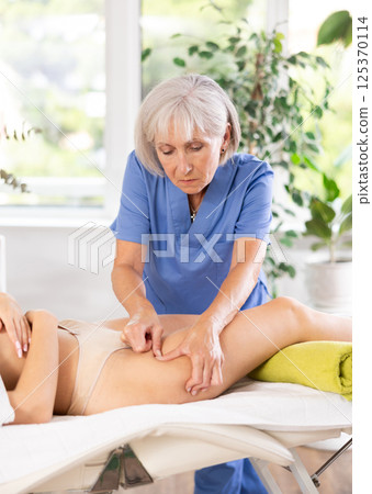 Experienced masseuse doing thigh massage to young female client Experienced masseuse doing thigh massage to young female client 125370114
