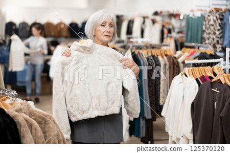 Elderly woman choosing fur coat in store 125370120