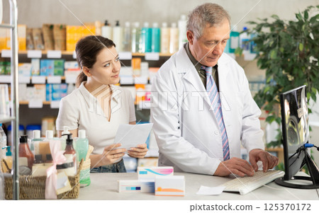 Male pharmacist helps female customer find prescription medication 125370172