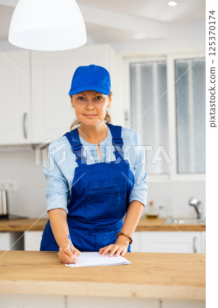 Woman house cleaner making notes in kitchen 125370174