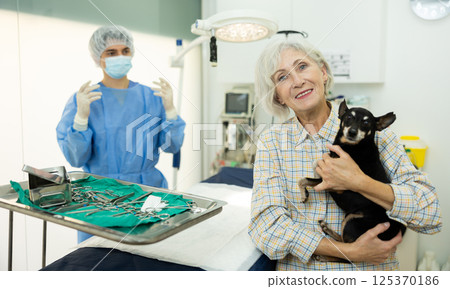 Smiling woman holding miniature pinscher in veterinary clinic operating room Smiling woman holding miniature pinscher in veterinary clinic operating room 125370186