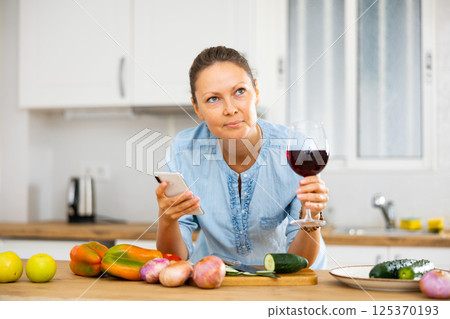 Woman with glass of wine in kitchen 125370193