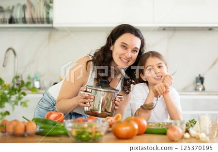 Mom and little daughter are standing at kitchen table with dishes in their hands. 125370195