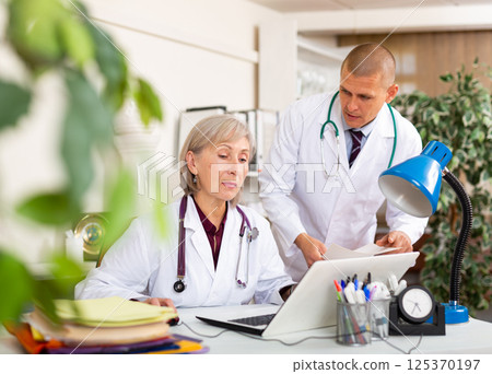 Elderly female doctor working in office with male colleague Elderly female doctor working in office with male colleague 125370197
