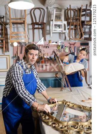 Portrait of middle-aged skillful repairman carpenter renovating mirror frame using tools in woodwork studio 125370215