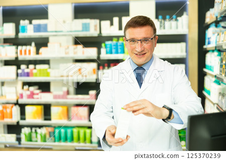 Middle-aged male pharmacist demonstrating preparation in box 125370239