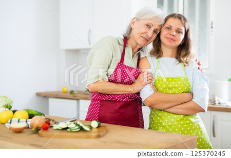 Portrait of cheerful elderly woman and her daughter in kitchen 125370245