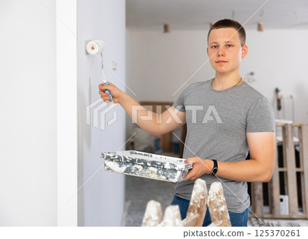Fifteen-year-old worker paints a wall with a roller 125370261