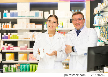 Two smiling female and male pharmacist workers stand shoulder to shoulder in apotheke 125370262
