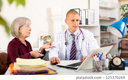 Focused doctor consulting aged female patient at clinic office 125370269