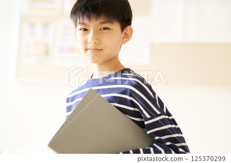 A male elementary school student smiling while holding a laptop 125370299