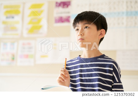 一名高年級男小學生拿著筆記本和鉛筆思考 一名高年級男小學生拿著筆記本和鉛筆思考 125370302