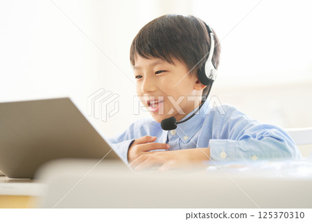 Elementary school boy smiling and talking while looking at a PC screen | Online learning image 125370310