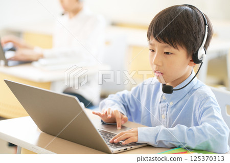 An elementary school boy wearing a headset and operating a PC An elementary school boy wearing a headset and operating a PC 125370313