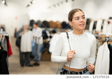 Young girl watching excitedly large stock of clothes in clothing store Young girl watching excitedly large stock of clothes in clothing store 125370316