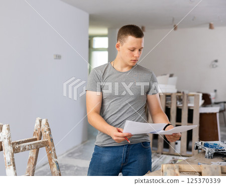Young man checking project documentation in apartment during repair works Young man checking project documentation in apartment during repair works 125370339