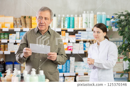 Female pharmacist helps an elderly man buy pills on doctor prescription Female pharmacist helps an elderly man buy pills on doctor prescription 125370346