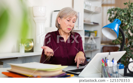 Upset frustrated elderly female entrepreneur sitting in office with laptop 125370353