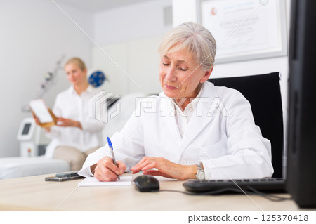 Senior woman dermatologist writing notes during appointment Senior woman dermatologist writing notes during appointment 125370418