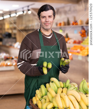 Man shop seller puts banana goods on display case Man shop seller puts banana goods on display case 125370420