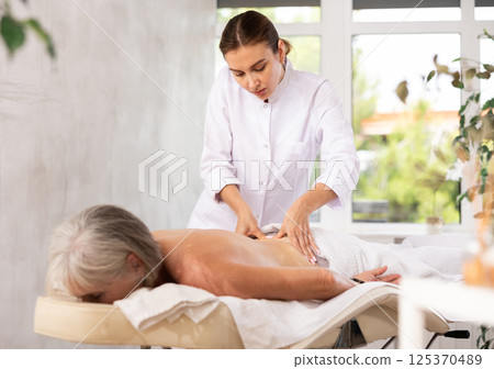 Young masseuse performing back massage to aged female client 125370489