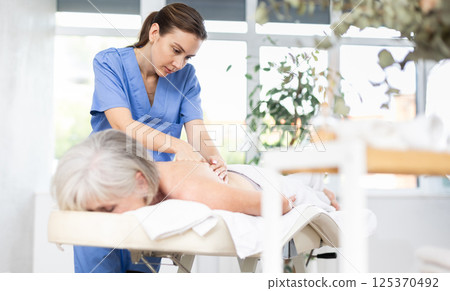 Professional young masseuse doing back massage to elderly woman Professional young masseuse doing back massage to elderly woman 125370492