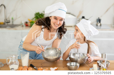 Happy mother and her daughter whisking ingredients in metal bowl in the kitchen 125370505