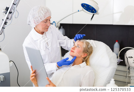 Young woman with mirror and cosmetologist after medical procedures 125370533