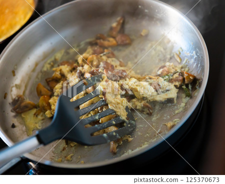 There is frying pan with scrambled eggs on stove, complemented with champignon and asparagus 125370673