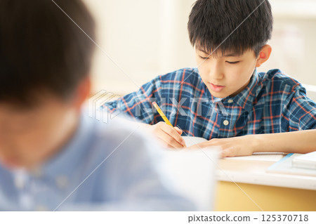 An elementary school boy writing with concentration | A serious expression as he concentrates on his studies 125370718