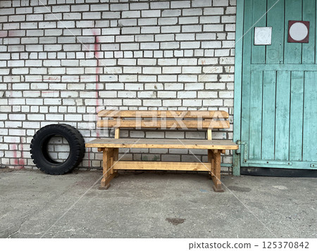 Wooden bench and tire by a brick wall near a teal door in an outdoor setting 125370842
