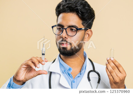 Indian young doctor man holding syringe needle and ampoule with liquid medicine treatment injection 125370960