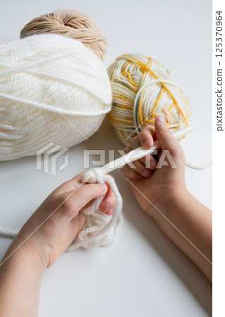 Child learning to crochet with white and yellow yarn skeins Child learning to crochet with white and yellow yarn skeins 125370964