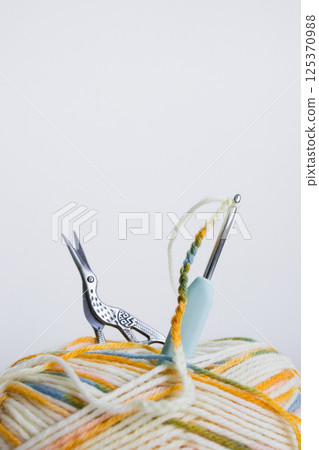 Multicolored yarn ball with crochet hook and scissors on white background 125370988