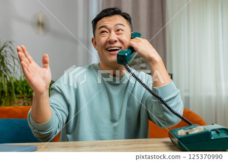 Asian man making retro telephone from 90s conversation call with friends on couch at home in room 125370990