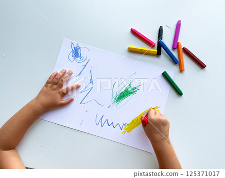 Child drawing with multicolored crayons on paper surface Child drawing with multicolored crayons on paper surface 125371017