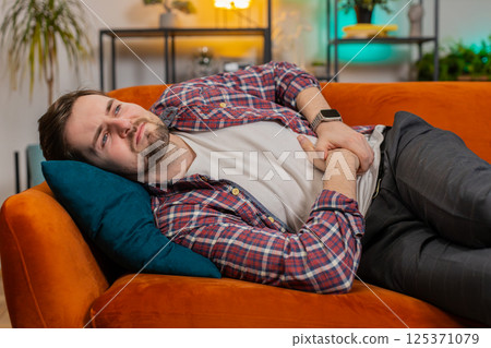 Man lying on sofa feeling sudden strong abdominal stomach ache gastritis problem poisoning diarrhea Man lying on sofa feeling sudden strong abdominal stomach ache gastritis problem poisoning diarrhea 125371079