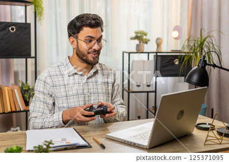 Indian businessman celebrating victory in video game on laptop clenching fists spending leisure time 125371095