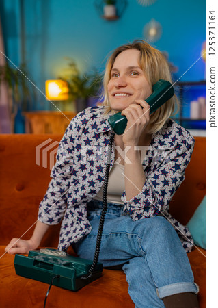 Smiling young woman making wired telephone call conversation with friends sitting on home couch Smiling young woman making wired telephone call conversation with friends sitting on home couch 125371164