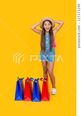 surprised teen kid with shopping bags on yellow background. full length and copy space 125371240