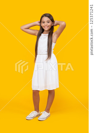 smiling teen girl in white dress standing on yellow background 125371241