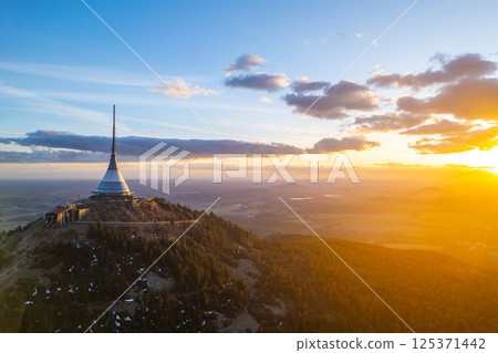 Springtime at Jested in Liberec offers breathtaking sunset views. The sun casts warm hues over the landscape, illuminating the iconic tower and surrounding nature. 125371442