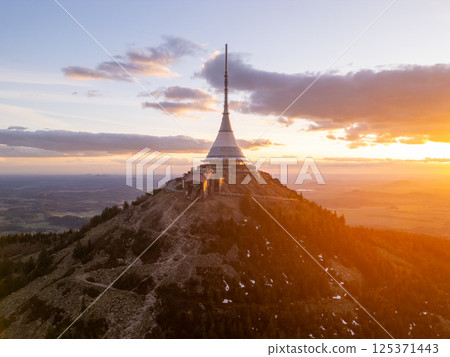 At sunset, the Jested mountain stands majestically in Liberec, Czechia, showcasing its iconic tower illuminated by soft golden light, surrounded by beautiful spring scenery. 125371443