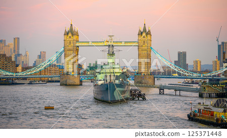 Tower Bridge stands majestically over the Thames River while HMS Belfast rests nearby during a serene evening in London, showcasing the beauty of this iconic location. Tower Bridge stands majestically over the Thames River while HMS Belfast rests nearby during a serene evening in London, showcasing the beauty of this iconic location. 125371448