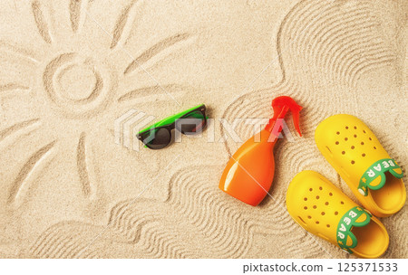 drawing on the sand, sun and waves,sunglasses, with an orange bottle, yellow rubber slippers, sun spray,on the sand, top view, no people, 125371533
