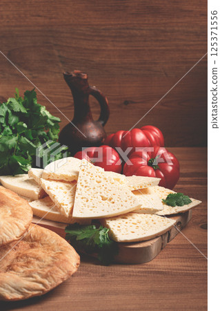 Georgian sliced cheese,on a wooden chopping board, with tomatoes with herbs and lavash, rustic style, Georgian cuisine, no people Georgian sliced cheese,on a wooden chopping board, with tomatoes with herbs and lavash, rustic style, Georgian cuisine, no people 125371556