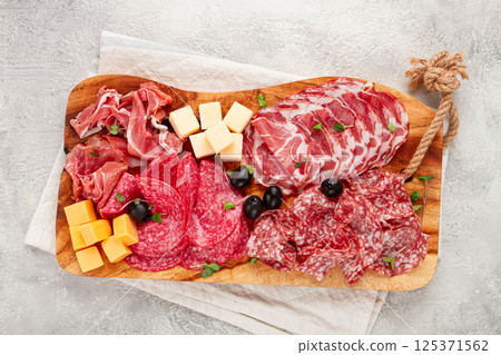 Assorted, sliced meat appetizer, prosciutto, salami and ham, with cheese and olives, on a wooden board, breakfast, top view, close-up, no people, 125371562