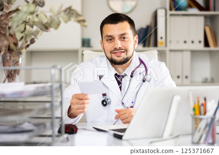 Man physician giving recipe, sitting at table in office Man physician giving recipe, sitting at table in office 125371667