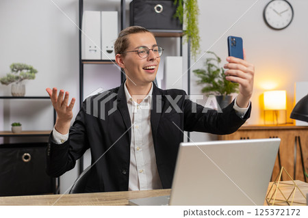 Happy businessman talking by online meeting conference video call using smartphone at home office 125372172